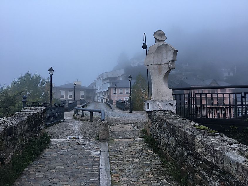 A pilgrim statue stands guard over a stone bridge on a foggy day. Part of the Camino Francés.