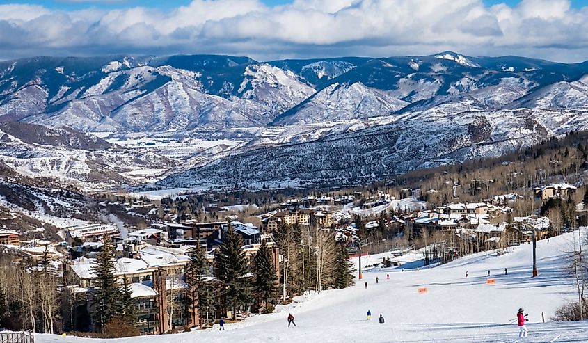 Panoramic view of Snowmass Village, with skiers skiing at the Aspen Snowmass ski resort in the foreground and the Rocky Mountains