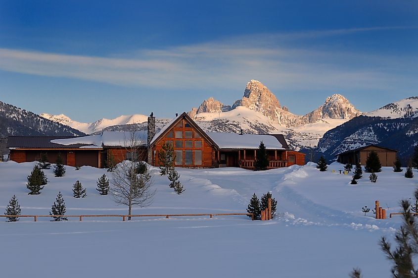 House in Driggs, Idaho, United States, captured on a winter evening with the Grand Teton peaks in Wyoming illuminated by sunlight at sundown.