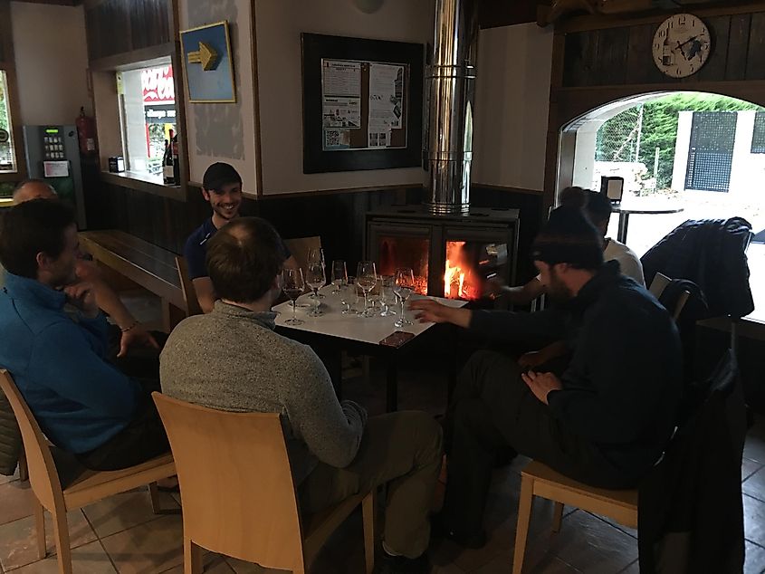 A group of men drinking wine and relaxing in front of an indoor fireplace. 